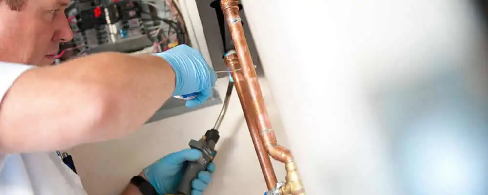 Water heater repair technician testing copper pipe connections and controls in Chattanooga, TN